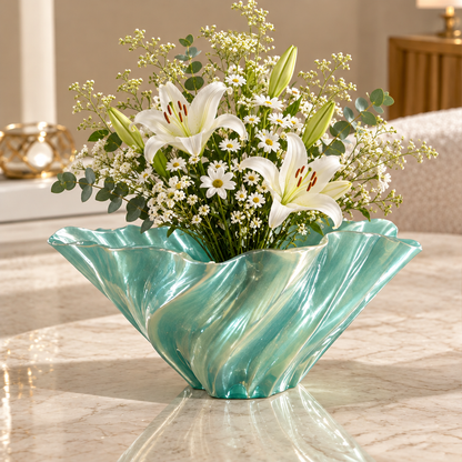 Aqua green sculptural wave vase with white flowers and greenery on a marble-look table.