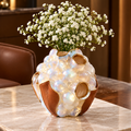Pearlescent bubble vase with brown leather panels and gold-toned rims, styled with tiny white flowers.