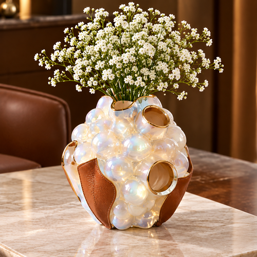 Pearlescent bubble vase with brown leather panels and gold-toned rims, styled with tiny white flowers.